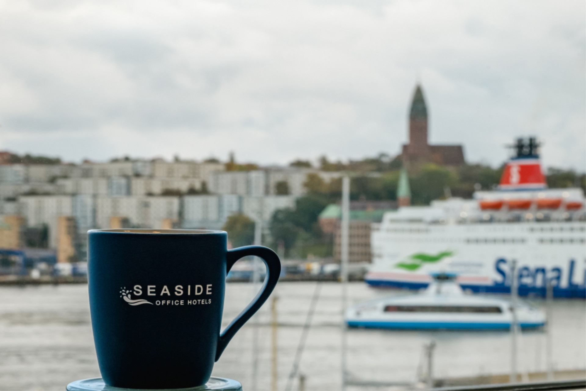 cup-seaside-office-hotels-lindholmen-goteborg Coffee mug with Seaside Office Hotels logo overlooking Gothenburg harbor and Stena Line ferry at Lindholmen.