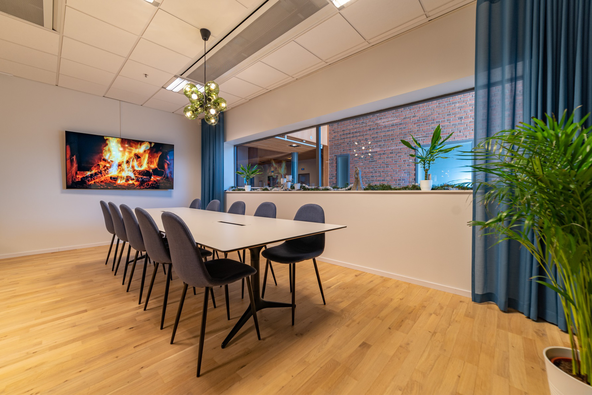 Stylish conference room at Seaside Office Hotels with modern chairs, large screen displaying fireplace, and indoor plants.