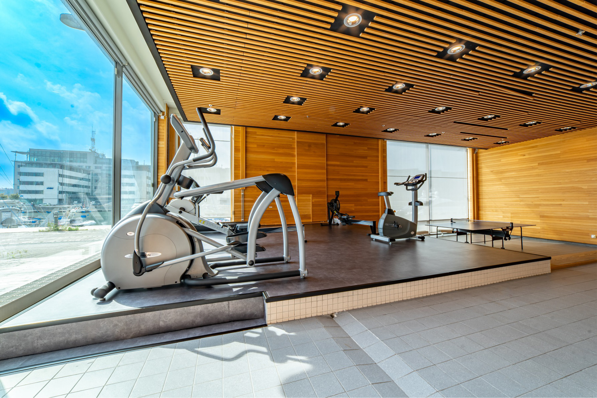 Cardio section of Seaside Office Hotels gym with elliptical, stationary bikes, panoramic windows, and wood-accented walls.