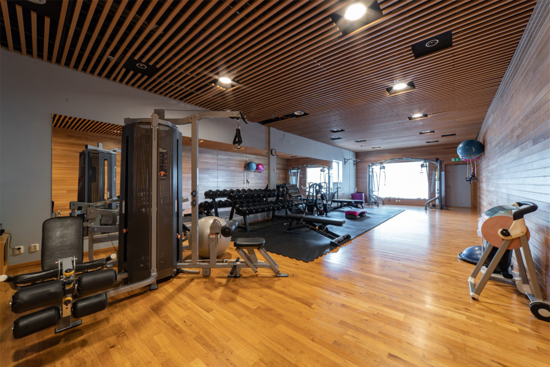Cardio section of Seaside Office Hotels gym with elliptical, stationary bikes, panoramic windows, and wood-accented walls.