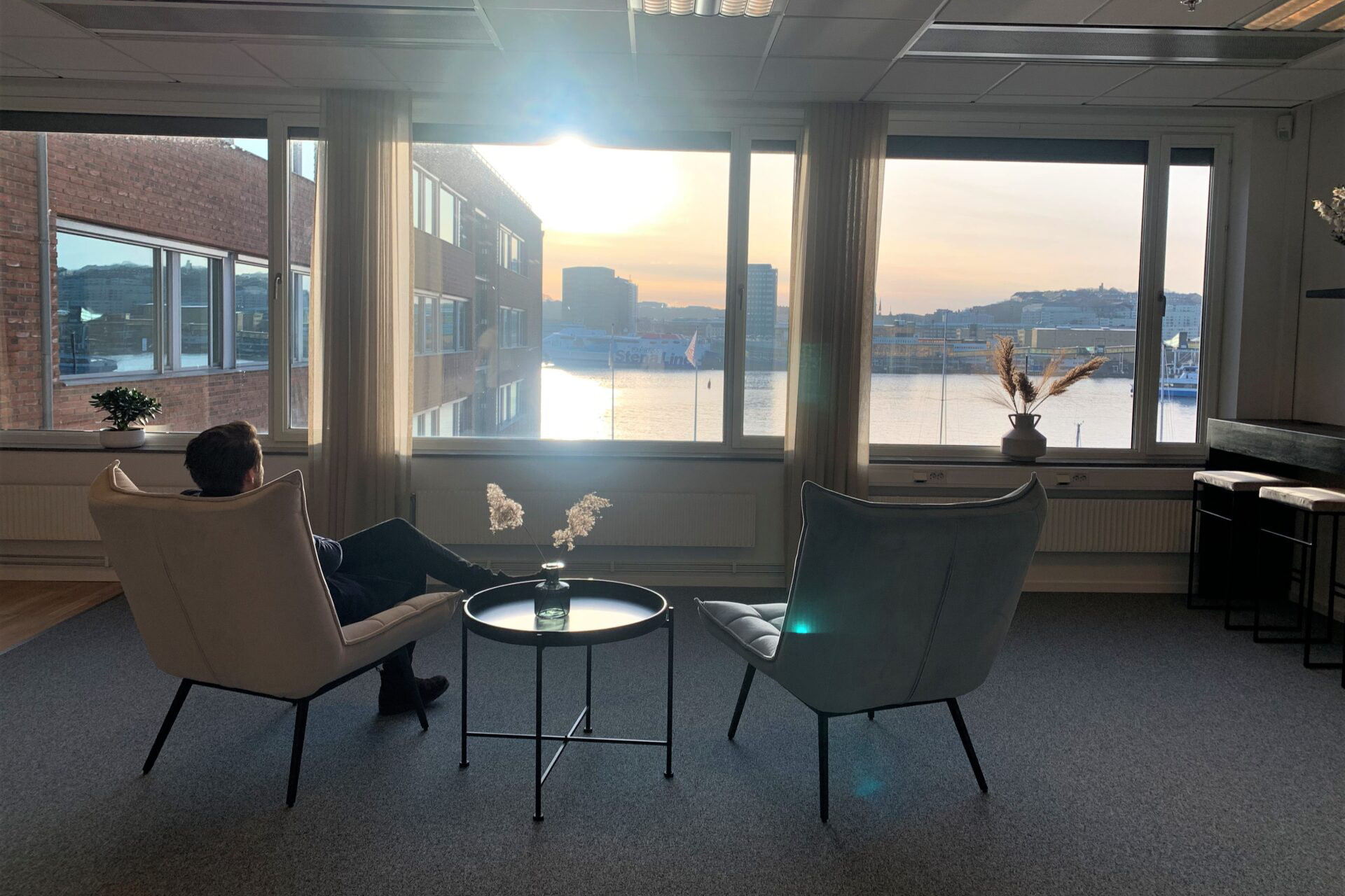 Relaxing lounge at Seaside Office Hotels with sea view, cozy armchairs, and scenic Gothenburg waterfront during sunset.